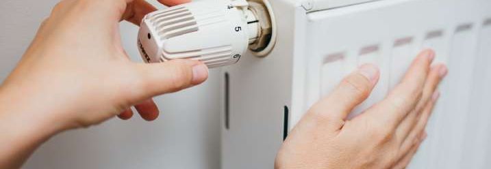 Nahaufnahme einer Hand, die an Thermostat die Heizkörpertemperatur einstellt